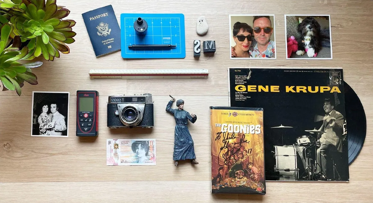 Flat lay of a passport, architect’s scale, vintage camera, laser measure, family photos and a Gene Krupa record