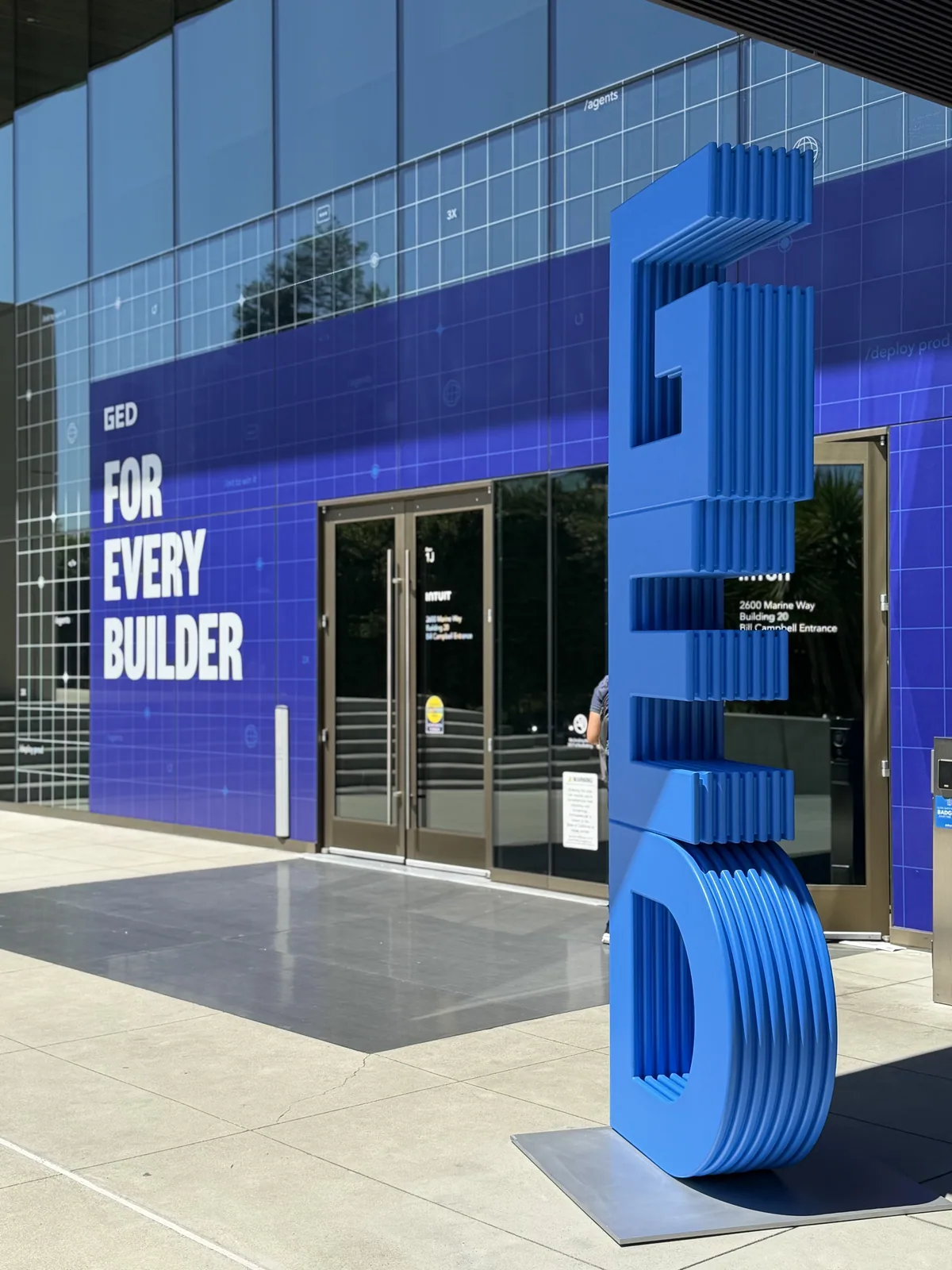 Building wrapped in a For Every Builder graphic beside a sculptural GED letterform