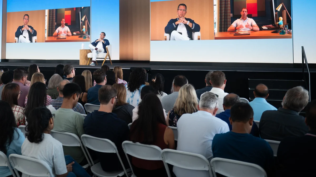 Leaders in conversation on stage, shown on the large screens